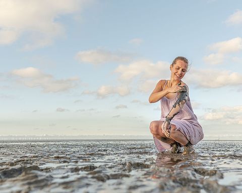 Frau im Watt, die ihre Arme mit Schlick einreibt